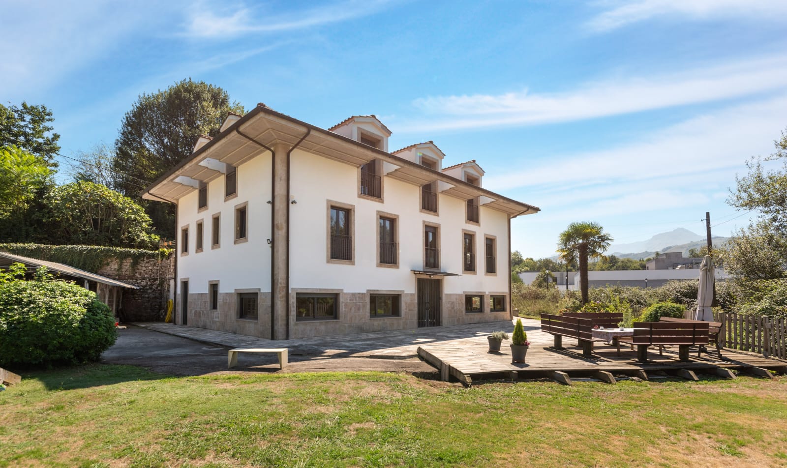 Fachada sur de la casa con el jardín y la terraza de madera